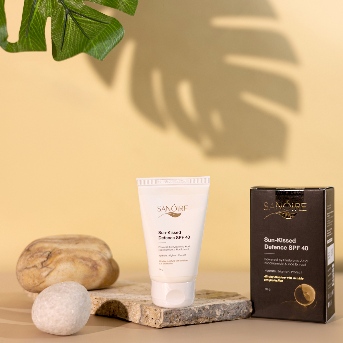 Sun-Kissed Defence SPF 40 sunscreen tube and box with rocks and leaf shadow on beige background