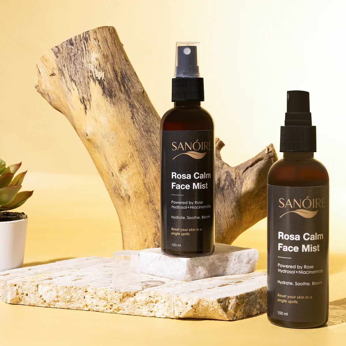 Two bottles of Rosa Calm Face Mist with natural stone and wood, skincare product display