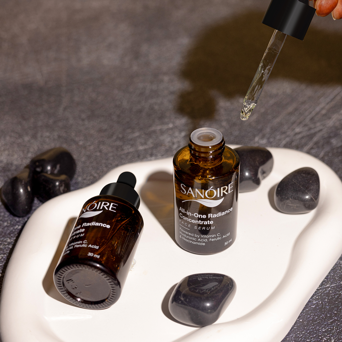 Face serum bottles with dropper on white dish, surrounded by black stones, skincare concept