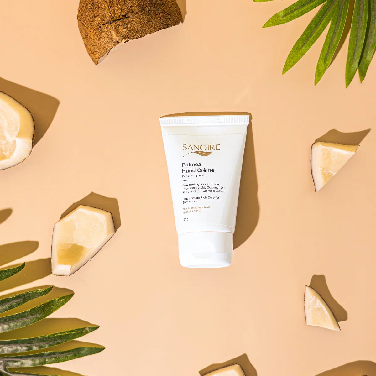 Palmea Hand Crème with SPF on beige background, surrounded by shea butter pieces and palm leaves