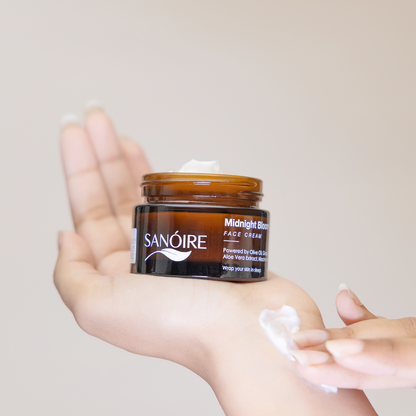 Hand holding Sanoire Midnight Bloom face cream jar with cream scooped on fingers