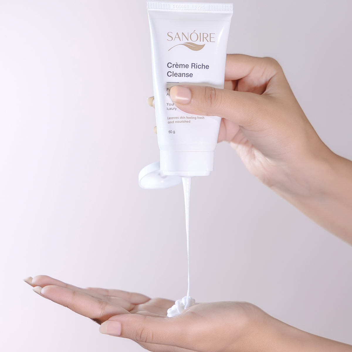 Person dispensing Sanoire Crème Riche Cleanse gentle face cleanser onto hand