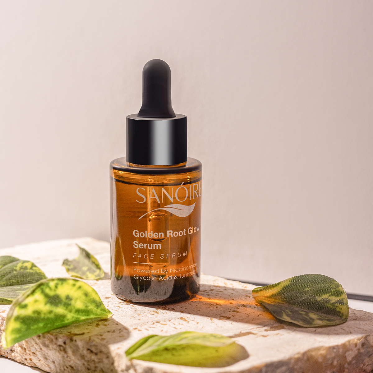 Golden Root Glow Serum dropper bottle displayed on stone with green leaves, skincare product