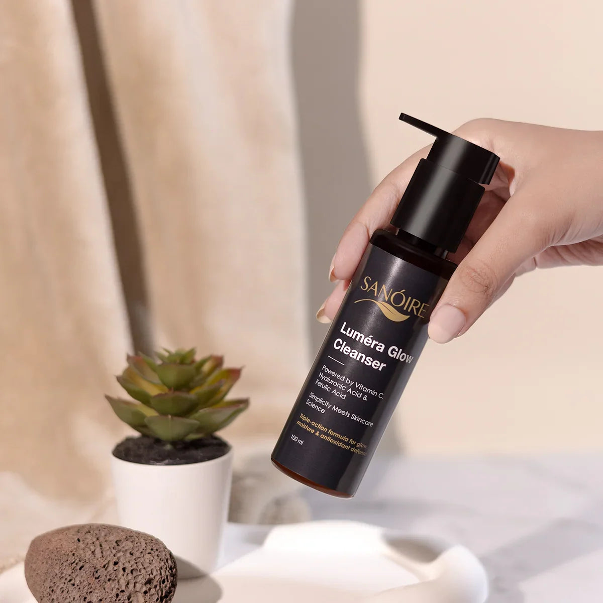 Hand holding Luméra Glow Cleanser bottle, skincare product with succulent and pumice stone