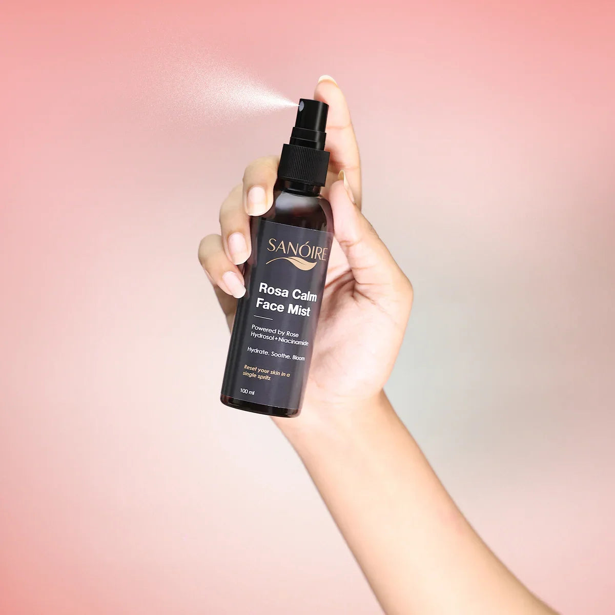 Hand spraying Rosa Calm Face Mist skincare bottle against a soft pink background