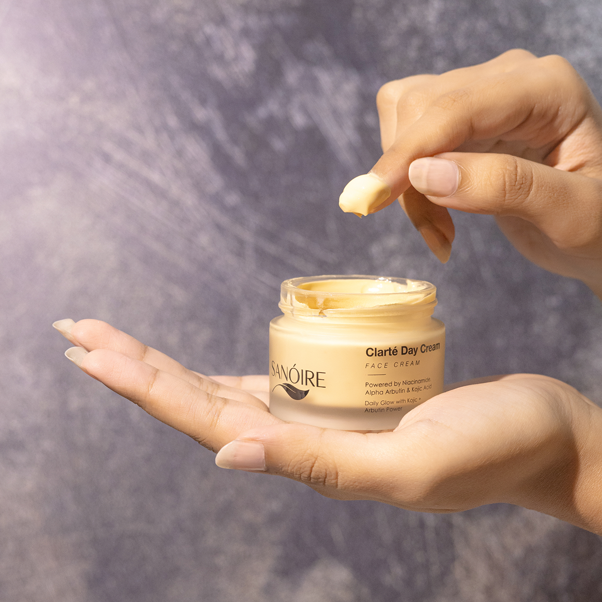 Hands applying Clarté Day Cream face moisturizer from an open jar against a soft background.