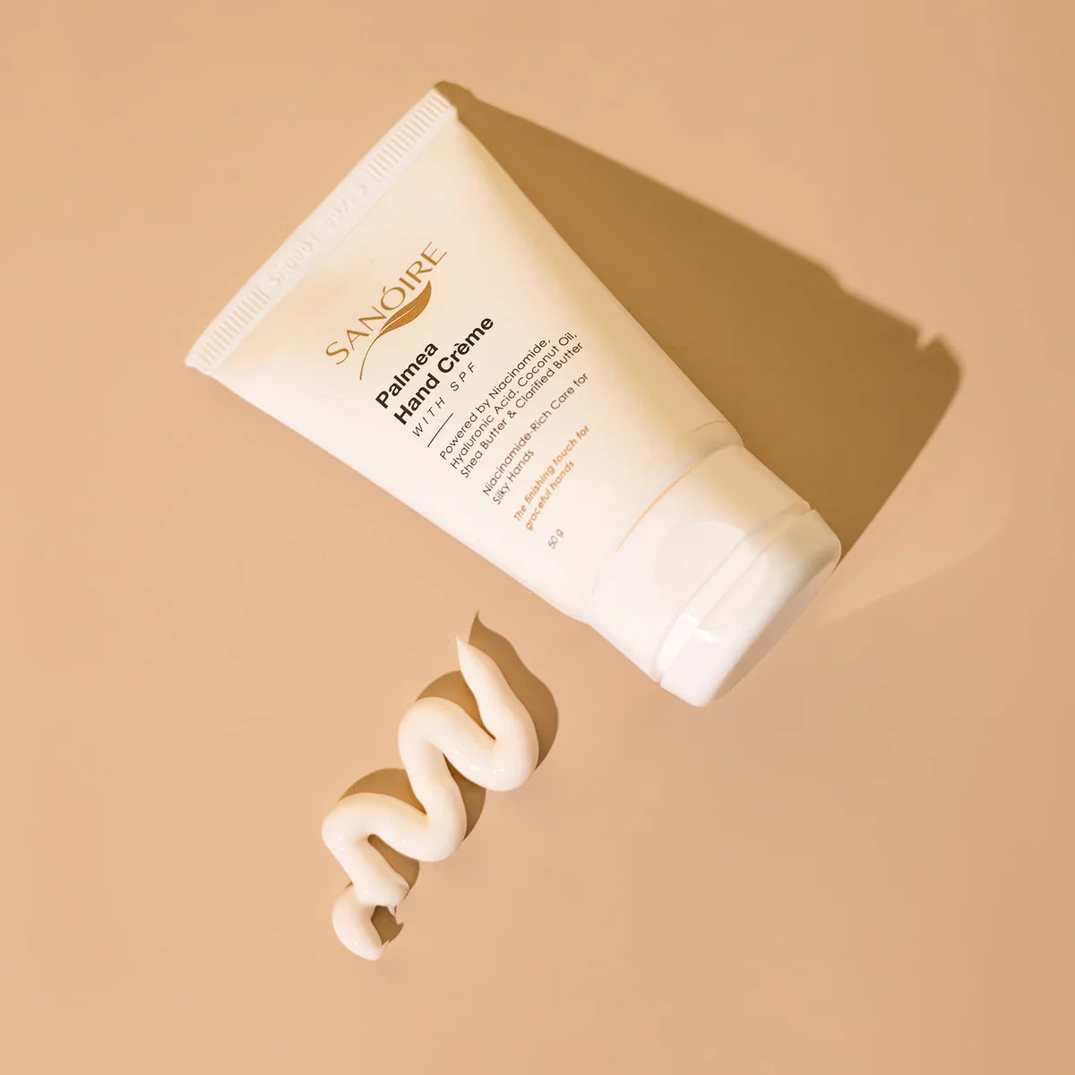 Palmea hand cream tube with SPF on beige background and creamy lotion swirl