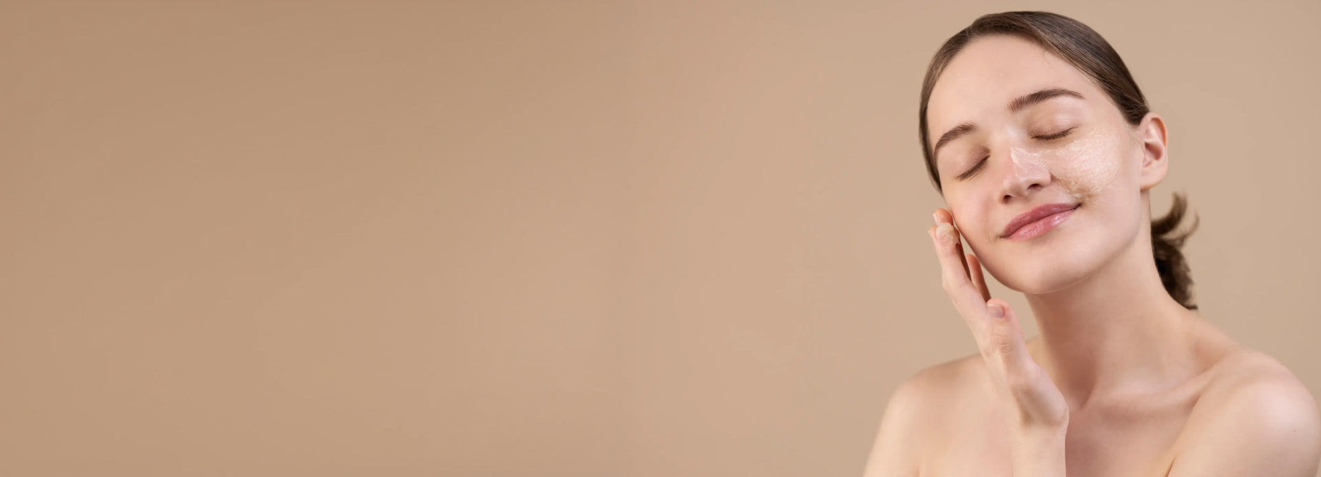 Woman applying facial skincare cream on cheek, healthy glowing skin, beige background