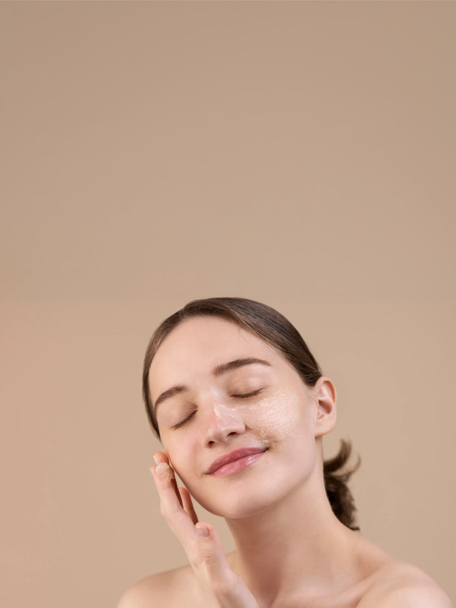 Woman applying creamy skincare product to face, natural healthy skin, beige background