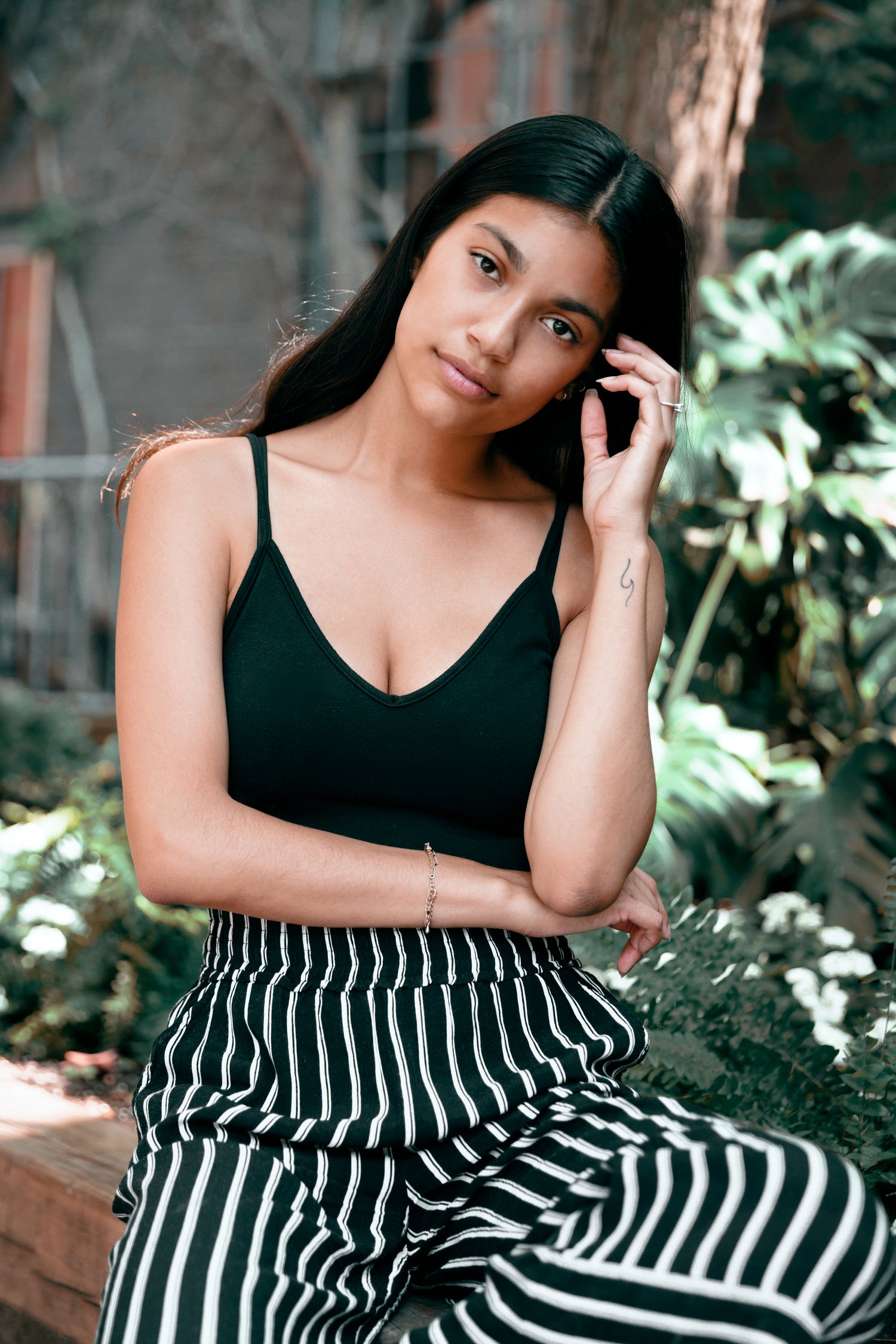 Woman with clear skin in black tank top and striped pants posing outdoors